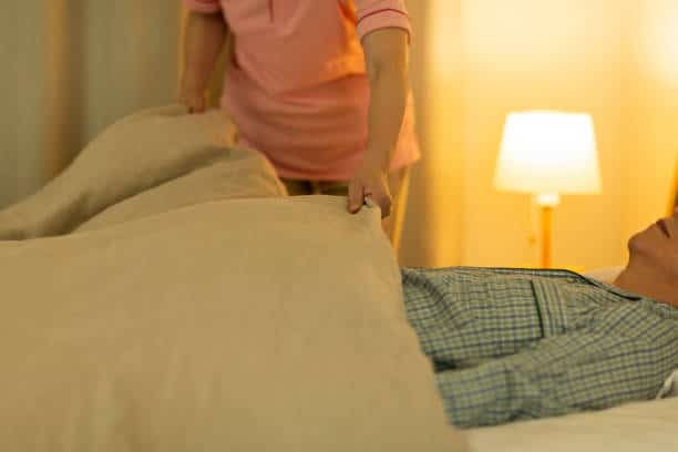 Night time care assistant - lady covering up a man with blanket